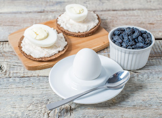 Boiled egg in egg cup and sandwich with cheese with slice egg, raisin, honey, parmesan, nut and pumpkin seed. Healthy breakfast on a wooden table