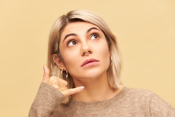 Close up image of pretty female with blonde bob hairstyle and nose ring looking up, holding hand at...