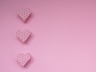 Row of pink handmade heart-shaped gift boxes on a pastel pink background (copy space on the right for your text, top view, minimal concept)