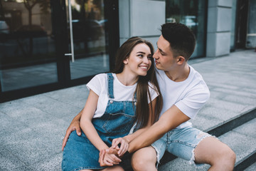 Positive male and female enjoying date time at urban setting embracing each other and looking in eyes, happy hipster guys communicating and smiling, concept of warm feelings and relationship