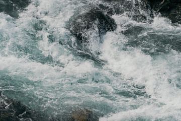 Strong mountain river. Rapid flow of stream among rocks. Blue stream of water seethes in rocks