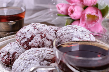 Delicious chocolate chip cookies covered with icing sugar on a vintage silver tray next to two cups of hot tea, a bouquet of tulips is visible from behind