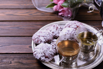 Obraz na płótnie Canvas Delicious chocolate chip cookies covered with icing sugar on a vintage silver tray next to two cups of hot tea, a bouquet of tulips is visible from behind
