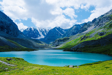 Naklejka na ściany i meble Turquoise lake among mountain peaks. High mountain river on summer day, hiking on rocks and stones