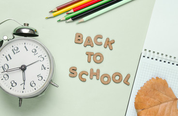 School time minimal concept. Notepad, colored pencils, alarm clock on mint green pastel background...