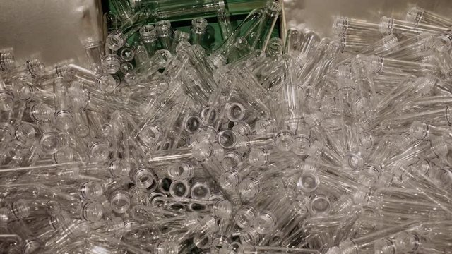 Conveyor belt with plastic molds and blanks in form of flasks for production bottles, dishes and containers on plant, closeup view. Manufacturing from secondary raw materials. Recycling of plastic.