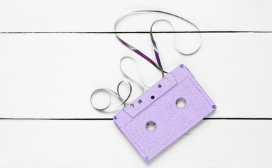 Music lover minimalism concept. Retro style 80s. Purple audio cassette with film on white wooden background.