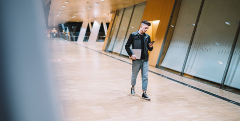 Confident young man using smartphone walking in hall