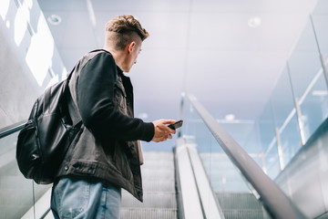 Hipster man with mobile phone on moving stairs