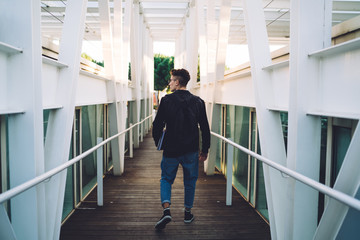 Young intern walking in hall and carrying laptop with documents