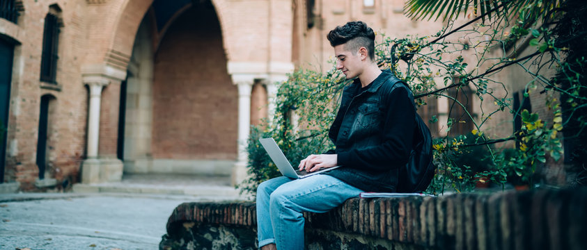 Young Man With Laptop Sitting On Stone Fence