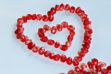 Pink pomegranate seeds placed in a heart shape on a white background