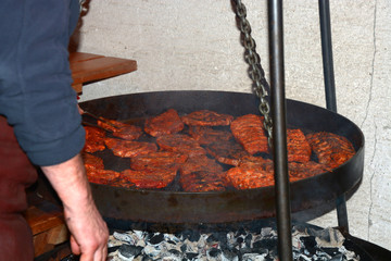 grill chef holding steel tongs and roasting steaks on big outdoor pan, grill master works on large pan and turns steaks