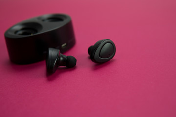 Obraz na płótnie Canvas Selective focus of black hand phone wireless earphones with charging station on pink background, isolated.Copy space.Gadget concept.