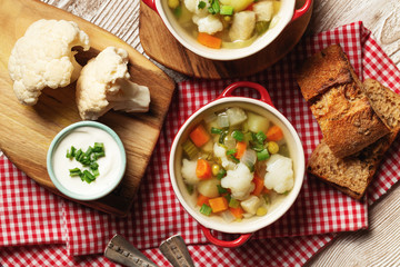 Cauliflower vegetables soup in bowl, bread, cream and raw cauliflower
