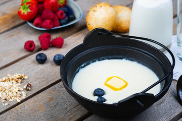 Traditional breakfast milk porridge with butter and berries on a wooden table.