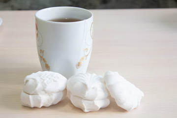 white marshmallow next to a mug of tea on a white table. lunch break.