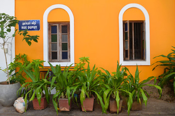 Beautiful french architecture of Pondicherry. Orange painted facade with wooden windows and green plants in clay pots at the street.