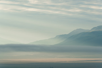 clouds and rays of dawn in mountain valley, soft light in early morning, meditation in nature. Gentle hills in bluish haze, silhouettes of mountains