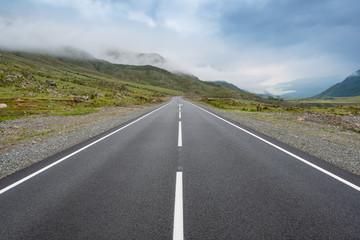 Asphalt road in mountain valley with ridge of rocks on horizon. Comfortable travel by car in wild