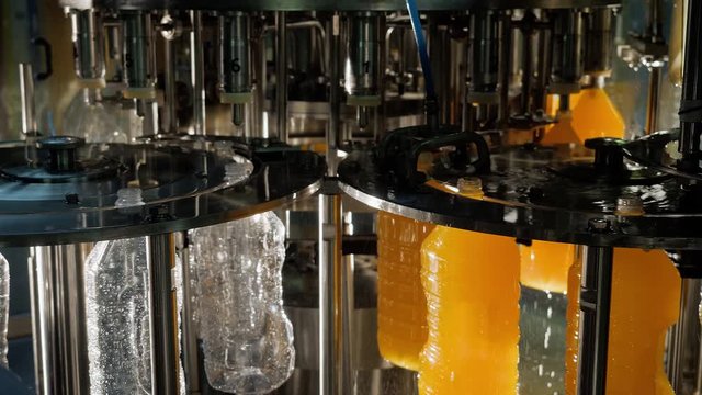 Process of production and bottling of juices, beverages in clean sterile plastic bottles on automatic conveyor line in shop on plant. Food industry concept. Manufactoring drinks on industrial factory.