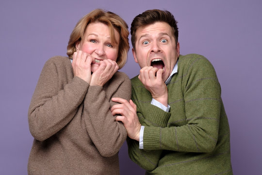 We are in awe. Scared man and woman coworkers being afraid biting nails standing on colored background. Studio shot.