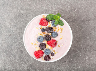 Berry smoothie bowl topped with blueberries, raspberry, blackberry, coconut flakes, yoghurt, muesli and mint for healthy breakfast, selective focus. Vegan food