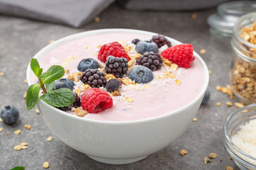 Berry smoothie bowl topped with blueberries, raspberry, blackberry, coconut flakes, yoghurt, muesli and mint for healthy breakfast, selective focus. Vegan food