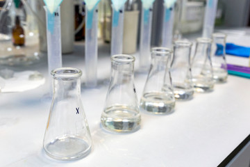 A long row of glass flasks with a clear liquid during a research experiment on a laboratory bench. The concept of modern science.
