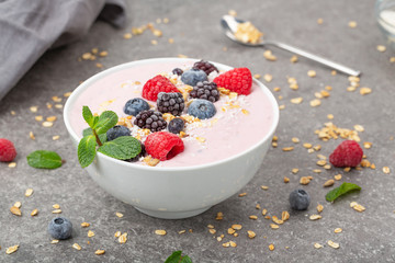 Berry smoothie bowl topped with blueberries, raspberry, blackberry, coconut flakes, yoghurt, muesli and mint for healthy breakfast, selective focus. Vegan food