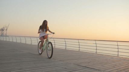Young beautiful woman with a bicycle is having a good time at the sea at sunset or sunrise 