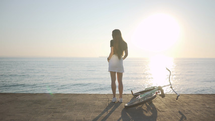 Young beautiful woman with a bicycle is having a good time at the sea at sunset or sunrise 
