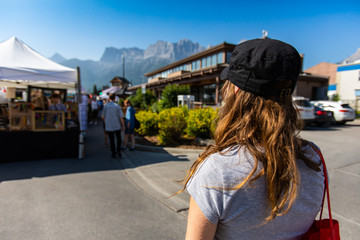 Fototapeta na wymiar A closeup and rear view of a slim caucasian girl with brunette hair and baseball cap during a local farmers market, with copy space on the left