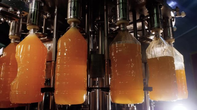 Manufacturing of soft drinks on industrial factory. Automatic conveyor line of bottling natural orange citrus juices in plastic bottles on plant. Food business concept. Production of fresh drinks.