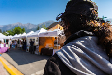 An over the shoulder view as a man in his early thirties walks towards market stalls during a local agriculture and artisan fair, with copy space