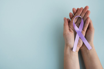 Womans hands hold lavender color awareness ribbon on a light background. World cancer day. Medicine...
