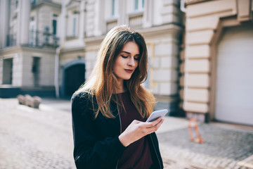 Attractive hipster girl outdoors  check mail by new cellular , woman sending text messages on modern mobile phone, female tourist searching news about places of  interest online walking on street