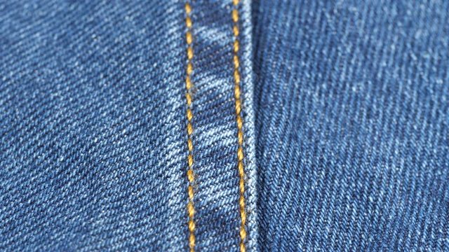 Seam on denim jeans, tracking macro. Denim textile texture, close up low angle. Slider shot. 4K 422 10 bit
