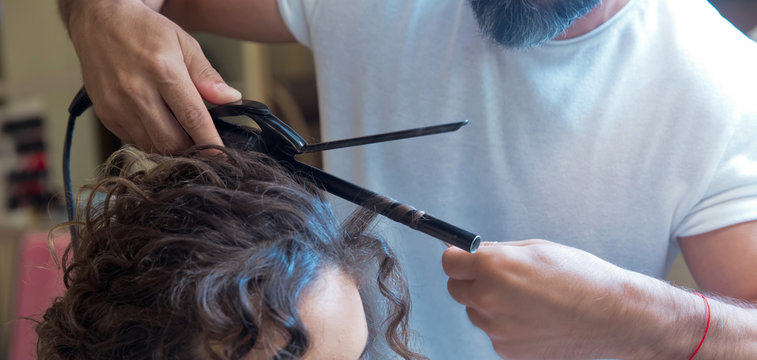 hairdresser straightening hair over . blonde doing the Curling irons in the beauty salon . Professional hairdresser . Close up of stylist's hand using curling iron working for woman client hair .