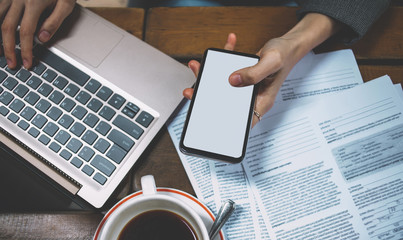 Close up top view of female hands holding smartphone with big screen front laptop keyboard working with documents at table. Sharing files via bluetooth between devices. Browsing network web via app