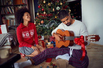 Fototapeta na wymiar Couple at Christmas morning sitting on floor and play guitar.