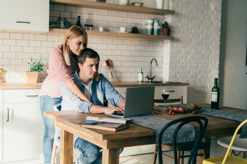 Woman embracing serious boyfriend working on laptop