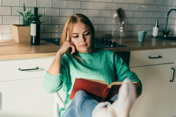 Young concentrated woman reading book with legs crossed