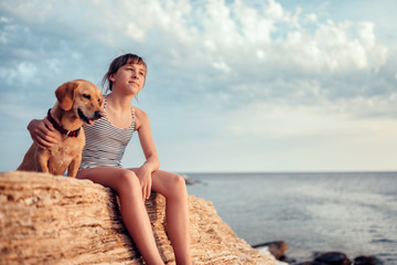 Girl embracing her dog while sitting on the rock by the sea