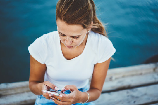 Charming hipster girl typing email message and searching information on website via cellphone outdoors,cropped image of  thoughtful woman checking balance using modern telephone at free time on lake