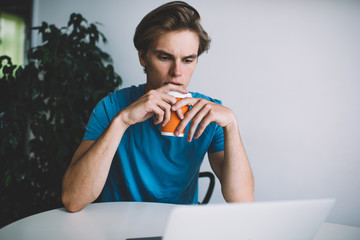 Puzzled hipster guy concentrated on received email from colleague during online messaging via laptop computer, serious Caucasian man in casual wear analyzing statistic of web blog during coffee time