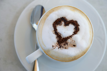 cup of cappuccino with cocoa powder in heart shape on a table in a street cafe, high angle view from above, selected focus, narrow depth of field