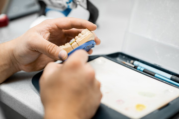 Dental technician coloring dental prosthesis with a paint brush at the laboratory, close-up view....