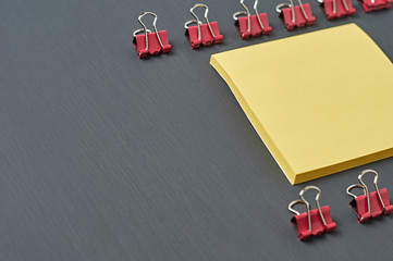 Rows of red metal binders near blank square paper for note lies on dark concrete desk in office, school or home. Space for text