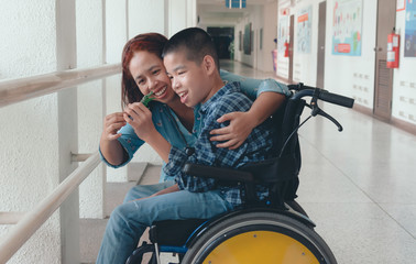 Mother and Asian special child on wheelchair is smile happily on background in school corridor, Life in the education age of disabled children, Happy disabled kid concept..